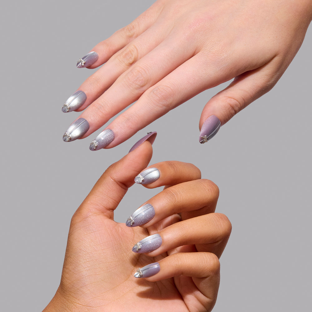 Two hands wearing Glamnetic Silver Stockings, featuring short almond nails with a silver metallic ombre finish and a small silver bow charm on each. - Product image