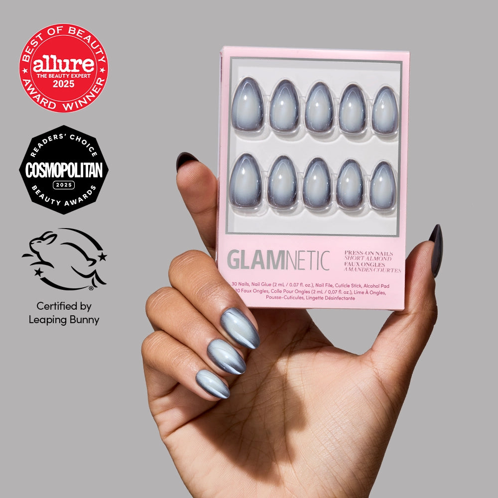 A hand with shiny silver press-on nails holds a box of glamnetic Smoke N’ Mirrors press-on nails. The box displays ten matching short almond nails, recognized for their salon-quality durability. Allure, Cosmopolitan, and Leaping Bunny certification logos appear on the left. - Product image