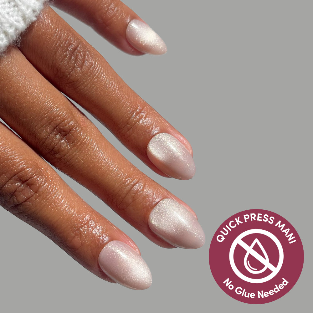 Hand with almond-shaped, shimmery light gray Snow Haze press-on nails next to a circular badge that reads Quick Press Mani, No Glue Needed, offering a salon-quality mani.