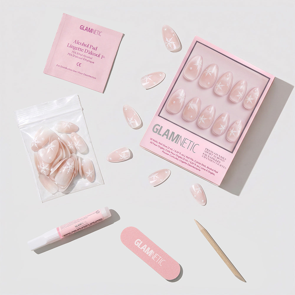 The Snowfall Press-On Nail Set by glamnetic features salon-quality pink nails adorned with chic white designs and a luxe velvet finish. The set includes an alcohol pad, nail glue, mini nail file, cuticle stick, and extra nails, all presented neatly on a white background. - Product image