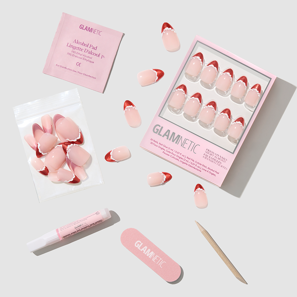Glamnetic Snow Kissed short almond press-on nails featuring red glitter tips and white scalloped edges, including a storage box, extra nails, an alcohol prep pad, nail glue, a file, and a wooden cuticle pusher. - Product image