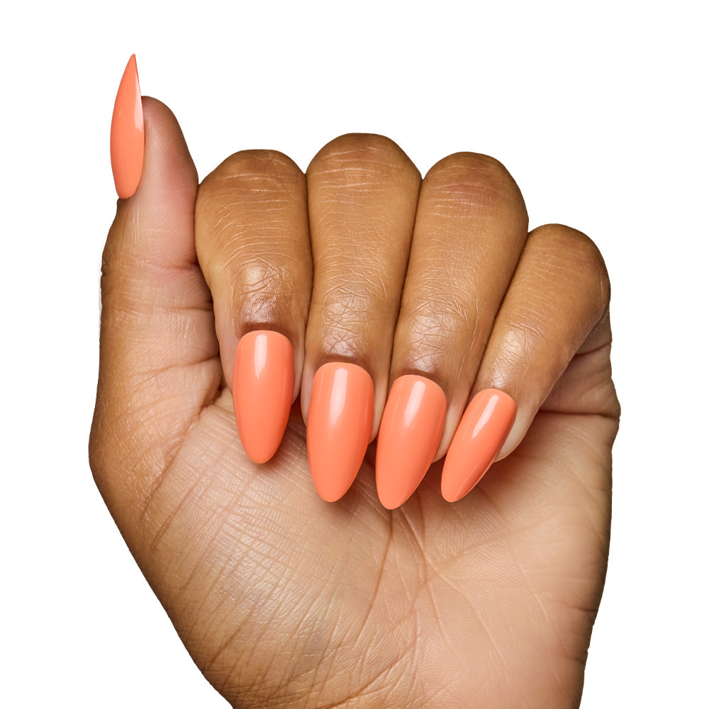 A hand with medium brown skin displays long, almond-shaped nails in glamnetic’s Soft Tangerine—a salon-quality acrylic look with a glossy pastel orange finish—set against a white background. - Product image