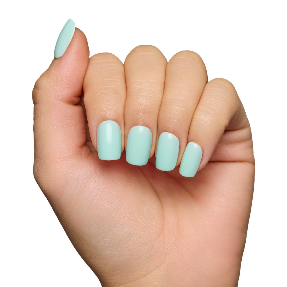 A light-skinned hand with fingers curled inward displays neatly manicured glamnetic Soft Teal Short Squoval Nails in a pastel mint green, set against a white background. - Product image