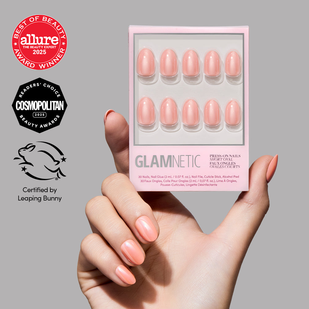 A hand with glossy peach-colored short oval press-on nails holds a box of Soft Skin nails from glamnetic. Award badges from Allure, Cosmopolitan, and Leaping Bunny are displayed on the left, highlighting this effortless nude manicure. - Product image