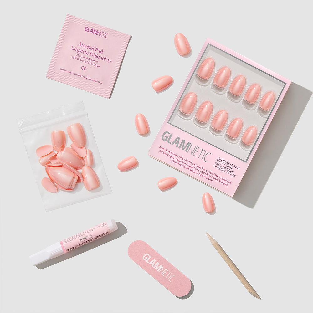 The Soft Skin press-on nails set by glamnetic includes nail glue, an alcohol pad, nail file, cuticle stick, and extra short oval nails—everything arranged on a light gray background for an easy nude manicure. - Product image
