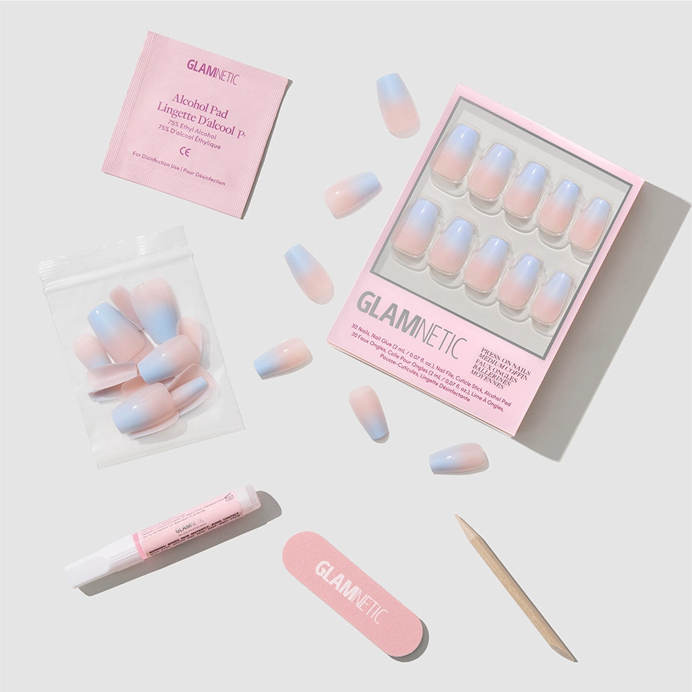 Introducing the glamnetic Soft Skyline Press-On Nails kit—a Nude-to-Blue Ombré coffin nail set that comes with nail glue, a wooden cuticle stick, a pink nail file, an alcohol pad, and extra nails, all elegantly arranged on a light gray background. - Product image