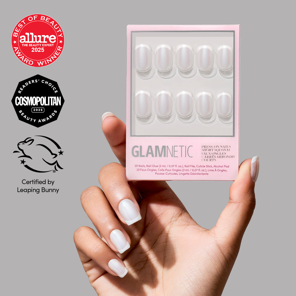 A hand with glossy, natural-looking short squoval nails holds a pink box of glamnetic Soft Tulle press-on nails. Award badges from Allure, Cosmopolitan, and Leaping Bunny are displayed on a gray background. - Product image