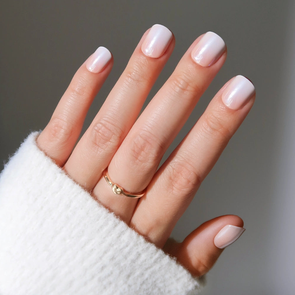 A hand with glamnetic’s Soft Whip nails—beautifully manicured in a nude-to-white ombré—is shown against a neutral background, paired with a cozy white sweater and a simple gold ring on the middle finger. - Product image