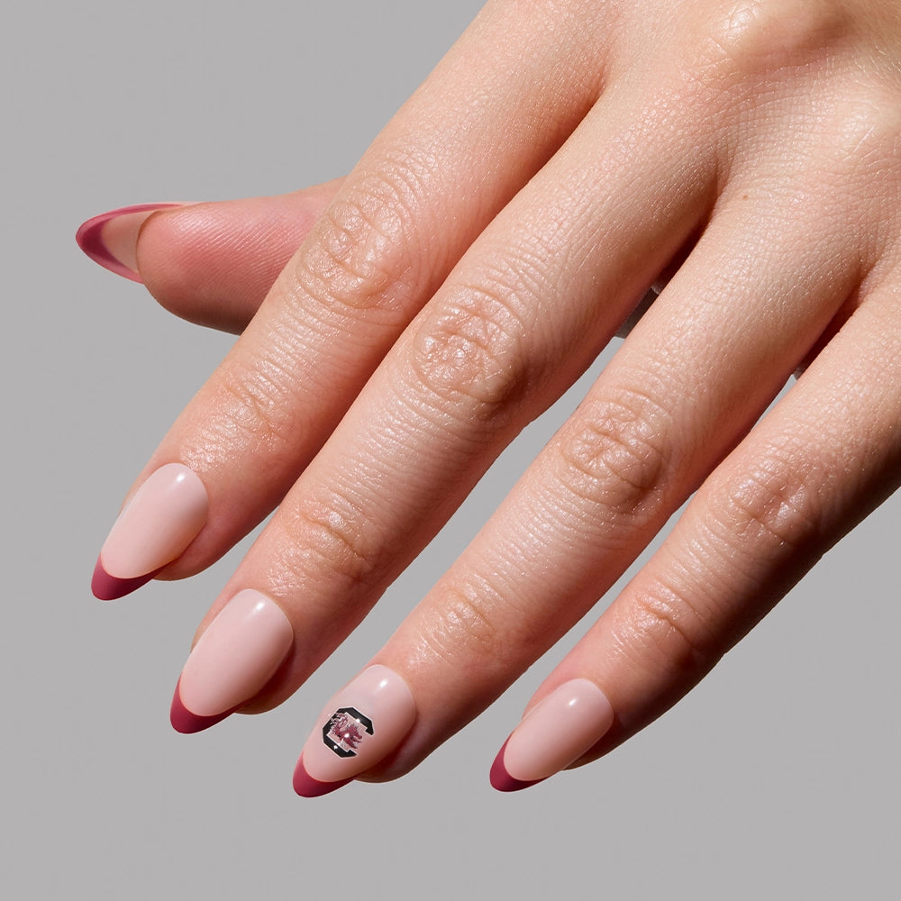 Show your team spirit with the glamnetic South Carolina Gamecocks Press-On Nail Set featuring long, almond-shaped nails with a nude base, deep pink tips, and a Gamecocks logo on the ring finger. - Product image