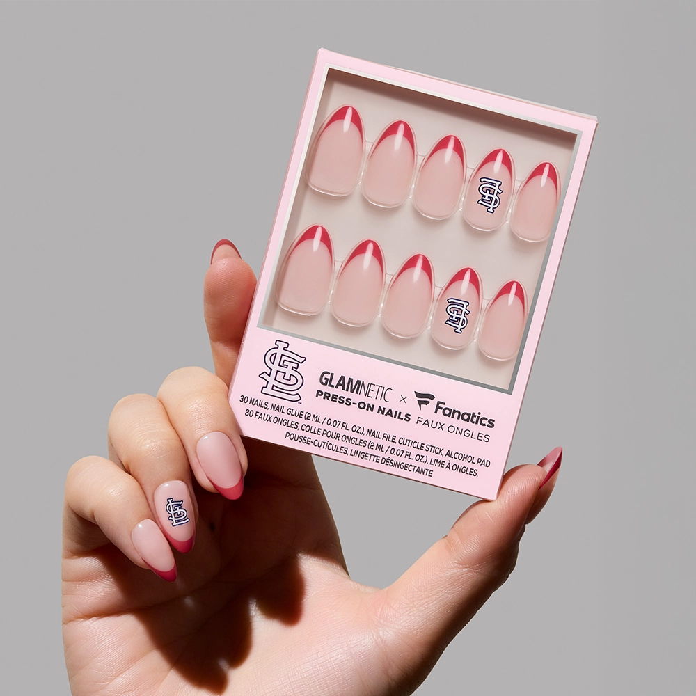 A hand displays one applied St. Louis Cardinals Press-On Nail from glamnetic, featuring pink French tips; the remaining nails are arranged in a pink glamnetic x Fanatics box.