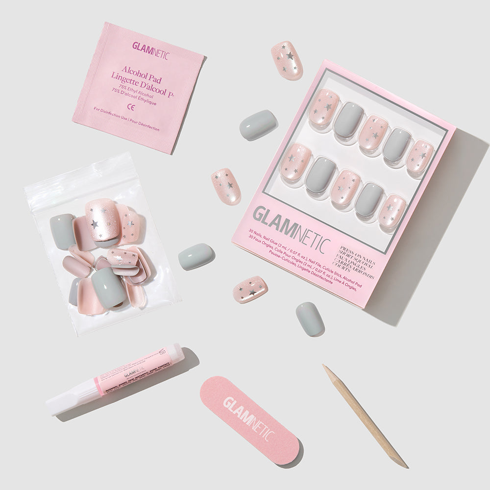 Starry Lights - Glamnetic Starry Lights press-on nails in a short squoval shape, featuring grey polish and glittery pink nails with silver star accents, displayed with nail glue, a file, a cuticle stick, and an alcohol prep pad.