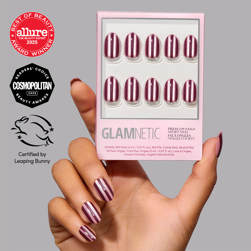 A hand holds a box of Glamnetic Sugar Stripes, vegan short oval press-on nails featuring a dark red and white vertical striped pattern, shown both in the packaging and on the nails. - Product image