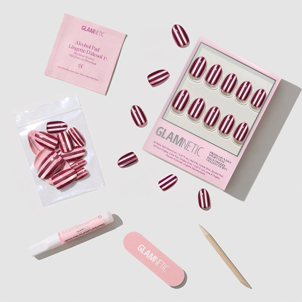 Glamnetic Sugar Stripes short oval press-on nails in a pink and burgundy striped pattern, including an alcohol pad, nail glue, a nail file, and a cuticle stick. - Product image