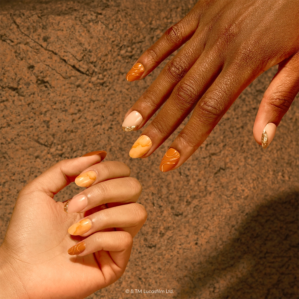 Two hands with almond-shaped nails, painted in the glamnetic Suns of Tatooine set’s orange, gold, and beige marble patterns, are held against a textured stone background. - Product image