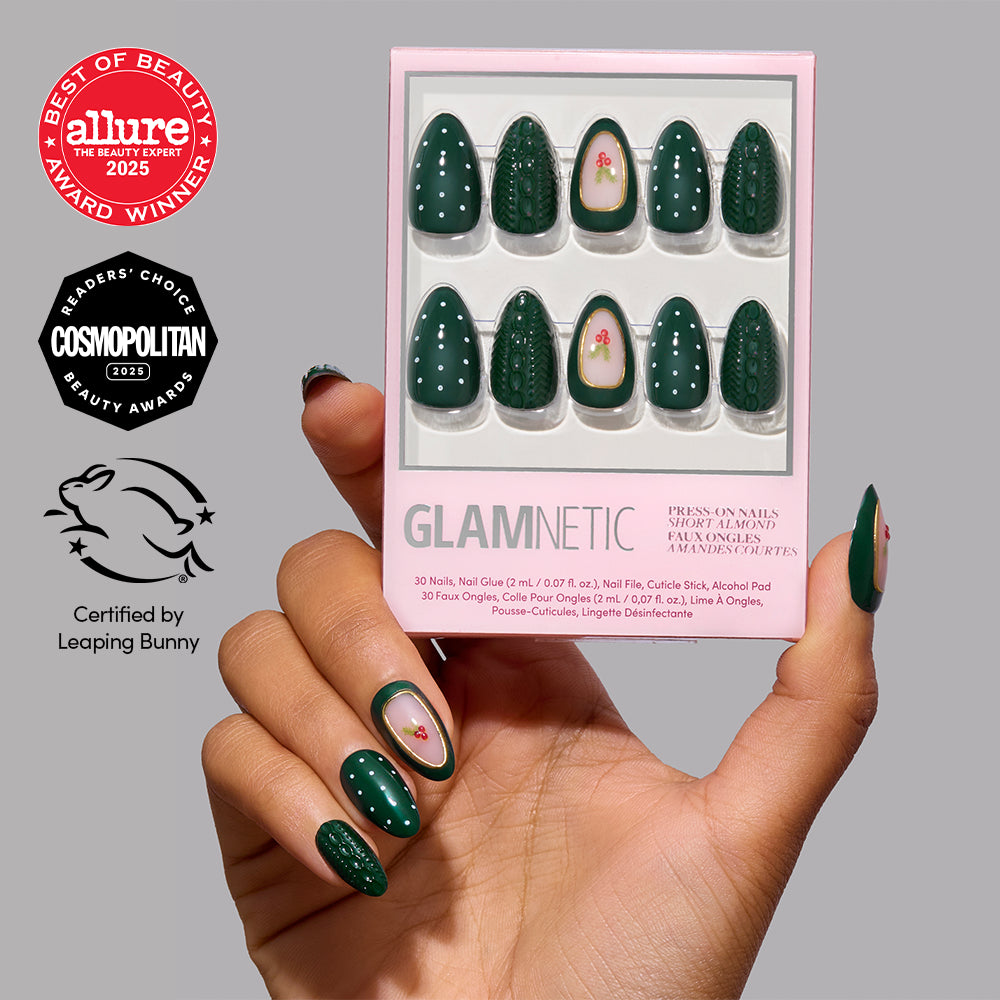 A hand holds a box of Glamnetic Table for Ten dark green short almond-shaped press-on nails featuring a textured cable-knit pattern and floral accents, surrounded by award seals and a Leaping Bunny certification logo. - Product image