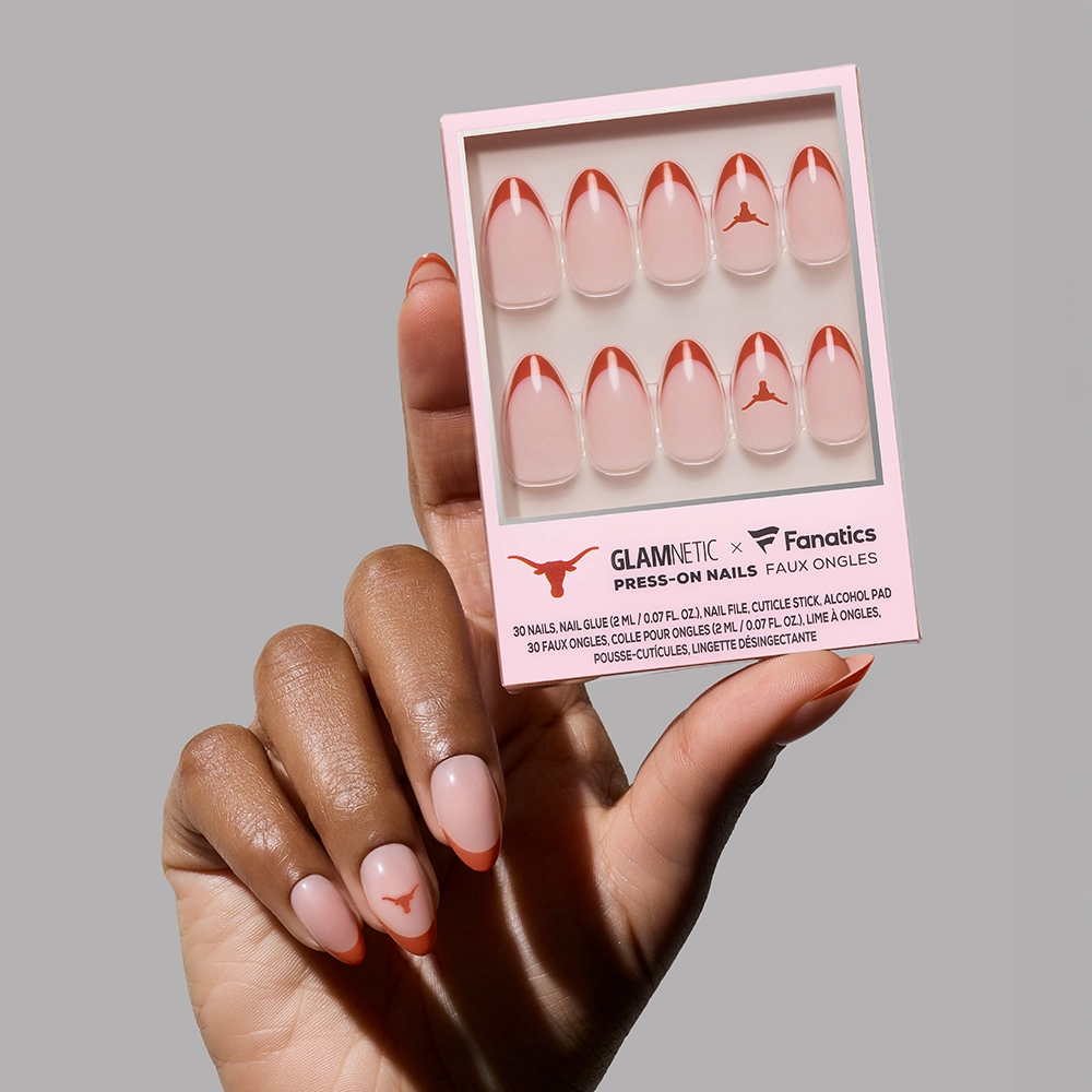 A hand with pink and orange French-tip glamnetic Texas Longhorns Press-On Nails holds a matching set in packaging, featuring the official logo and “GLAMNETIC x Fanatics Press-On Nails” text.