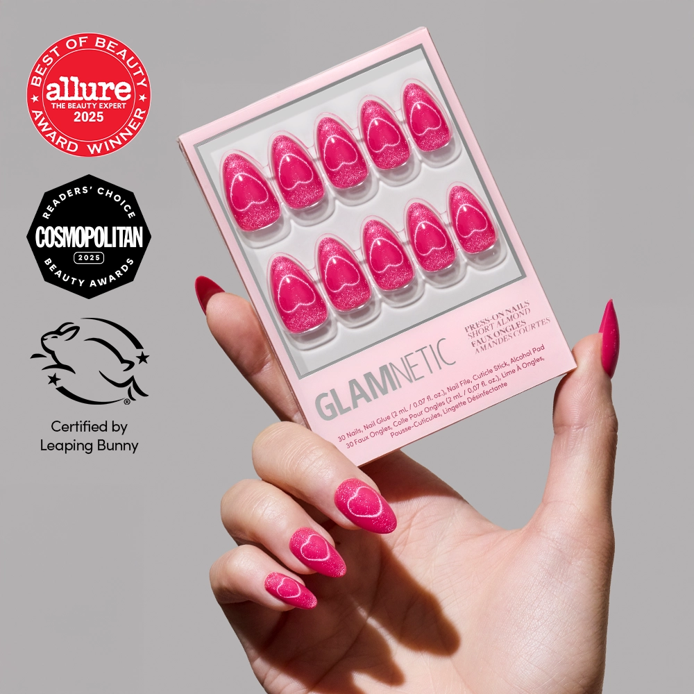 A hand with glossy pink, heart-patterned press-on nails holds glamnetic’s Text Me Back nail set. Beauty award logos from Allure and Cosmopolitan, plus a Leaping Bunny cruelty-free certification, are displayed on the left.