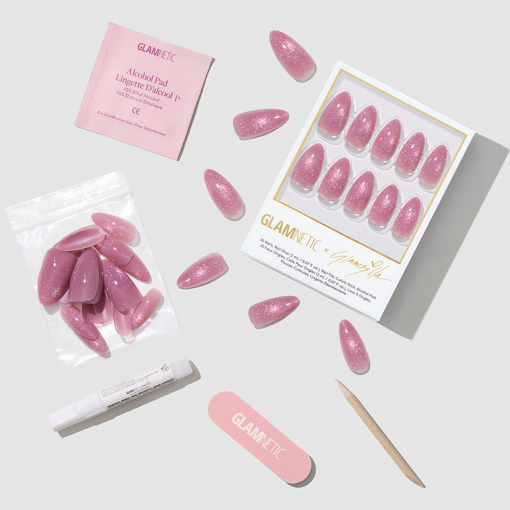 THE BEAUTY BLUEPRINT by glamnetic: pink glittery almond press-on nails with extra nails, alcohol pad, nail glue pen, nail file, and cuticle stick—all neatly arranged on a light gray surface. - Product image