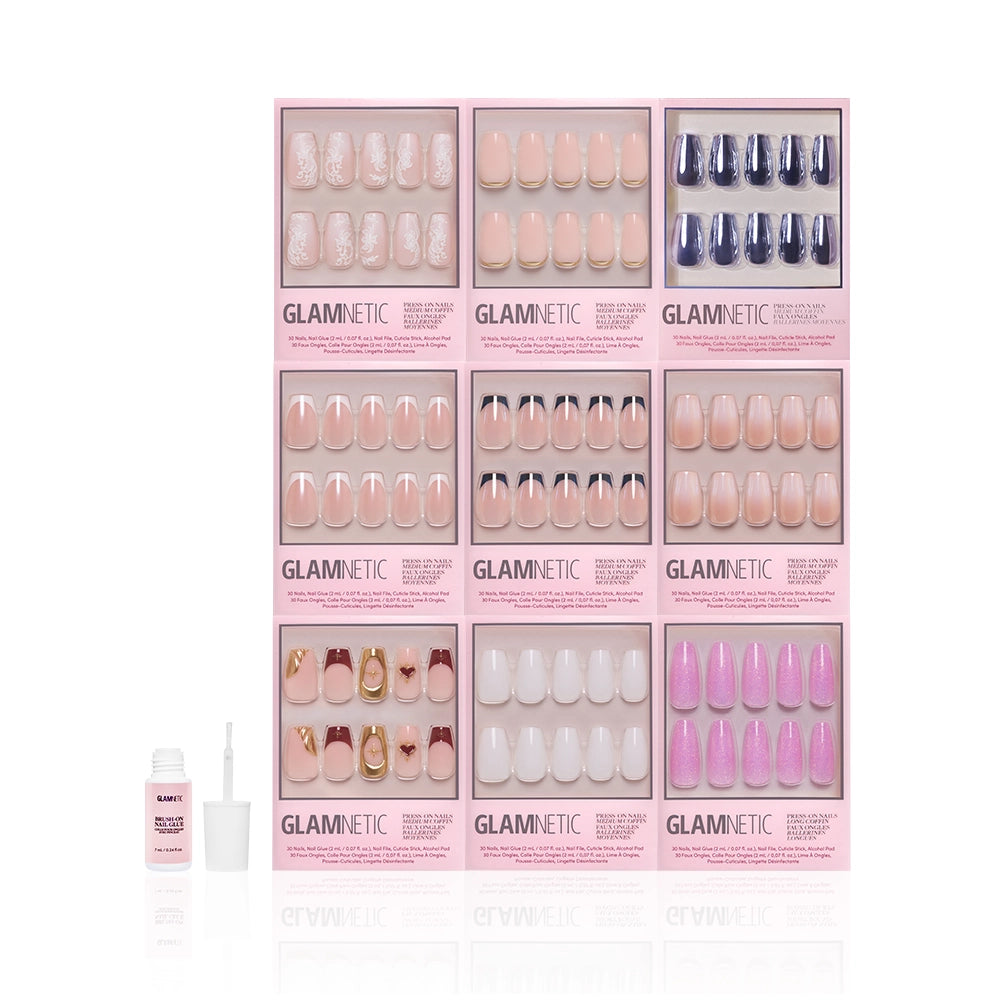 Nine glamnetic The Coffin Vault press-on nail sets in assorted coffin and neutral designs—pink, nude, blue, gold, glitter—are arranged in a grid. A nail glue bottle with applicator is placed in front of the sets. - Product image