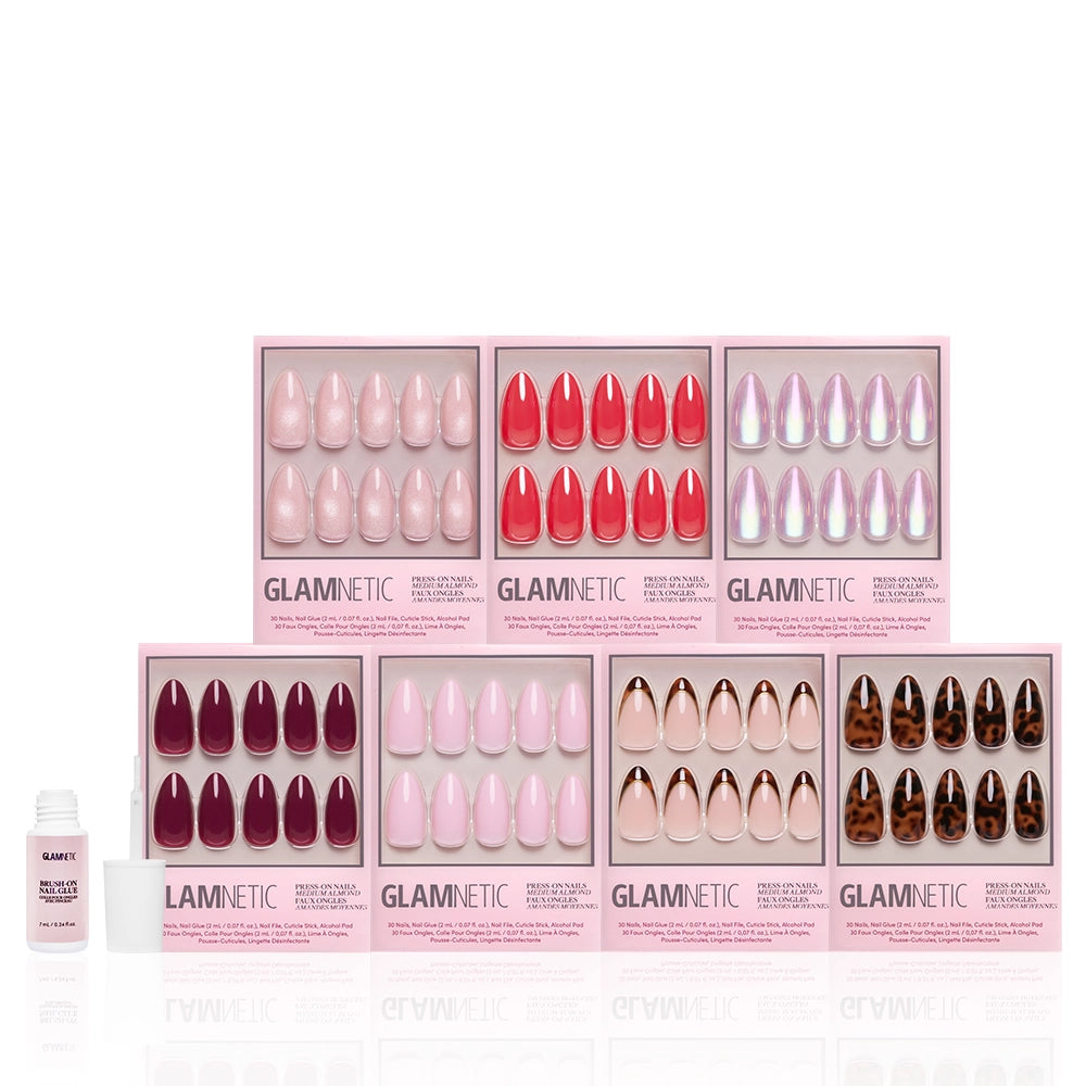 Seven boxes of glamnetic's The Medium Almond Edit press-on nails are arranged in two rows, with an open bottle of glamnetic nail glue to the left, all displayed on a white background. - Product image