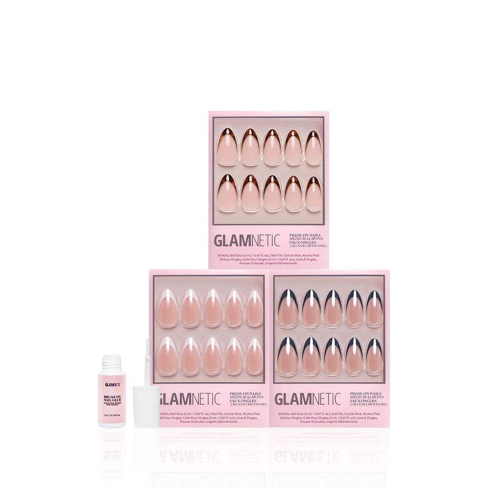 Three pink boxes of glamnetic's The Medium Almond Frenchies press-on nails in nude shades and almond shape are arranged in a triangle, with an open bottle of nail glue to the left on a white background. - Product image
