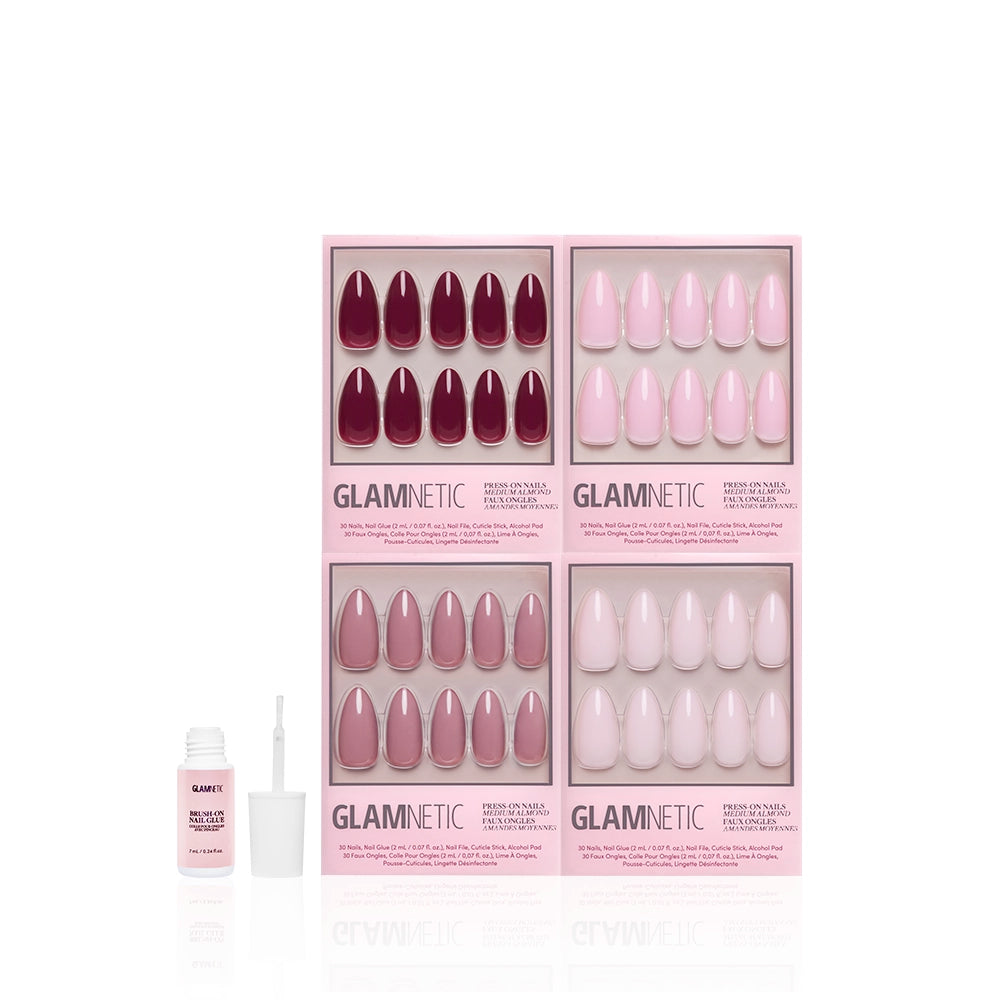 Four sets of glamnetic "The Pink Medium Almond Icons" press-on nails in burgundy, mauve, and glossy pink are shown in pink Glamnetic boxes. A small open bottle of nail glue is placed to the left of the pink nail set. - Product image