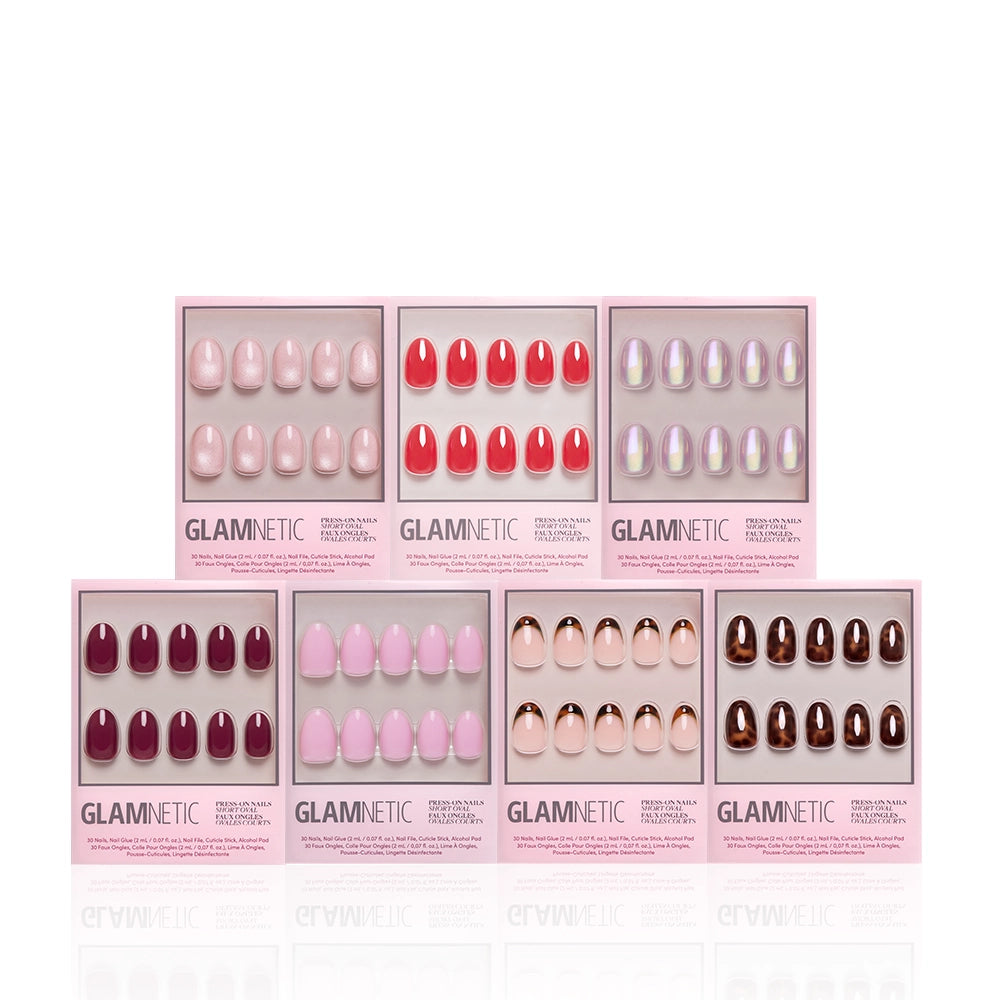 Seven boxes of glamnetic’s The Short Oval Edit press-on nails, featuring pink, red, nude, metallic, and iridescent finishes and a mani bundle, are arranged in two rows on a white background. - Product image