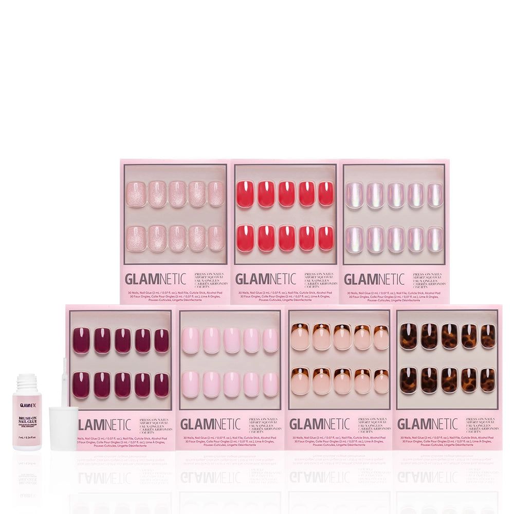Seven Glamnetic The Short Squoval Edit nail bundle sets—short squoval press-ons in assorted designs—are arranged in two rows with a nail glue bottle on the left. Pink packaging features clear windows to display each set. - Product image