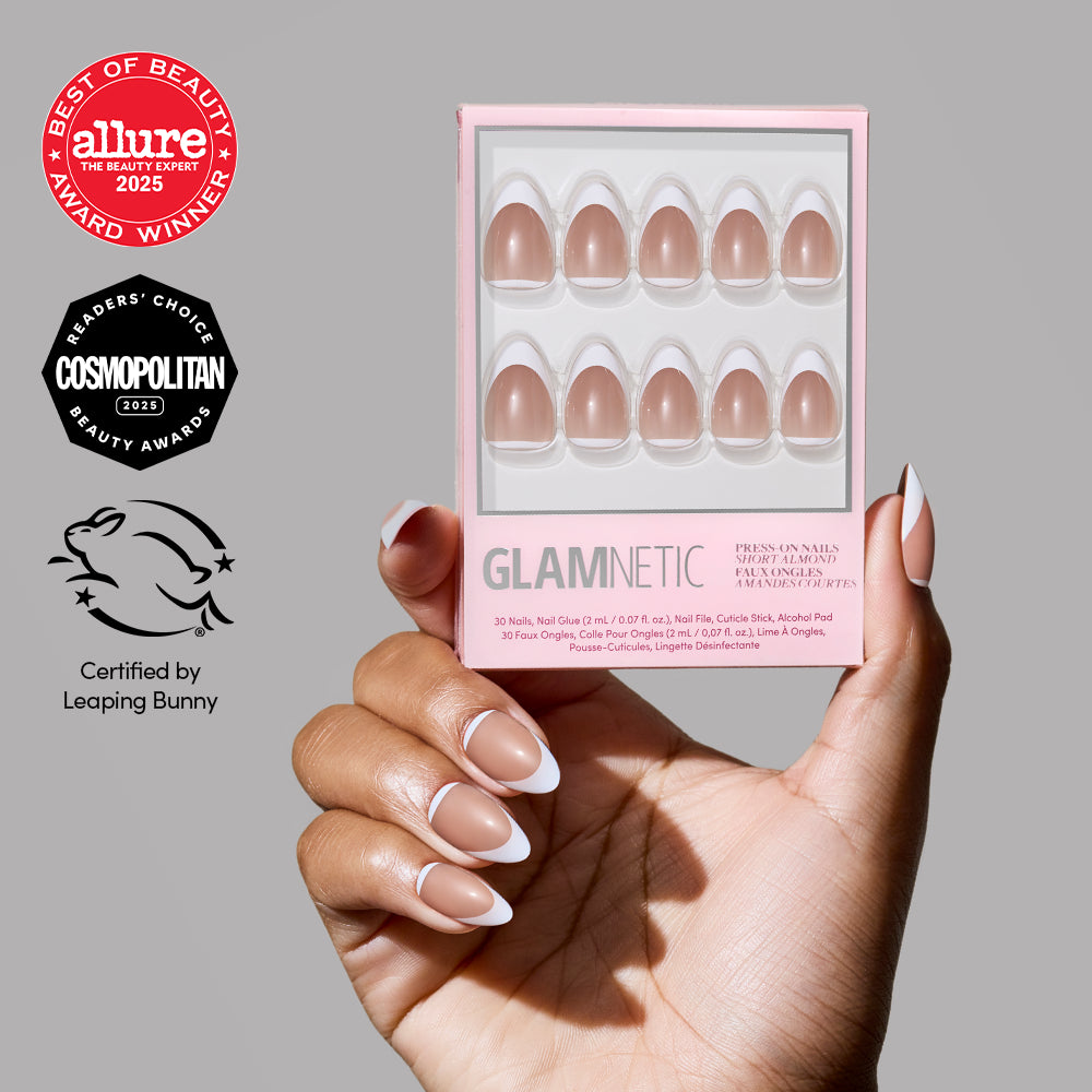A hand with manicured short almond nails holds a box of glamnetic Class Act French tip press-on nails in nude pink. Allure, Cosmopolitan, and Leaping Bunny vegan manicure certification logos appear on the left against a gray background.