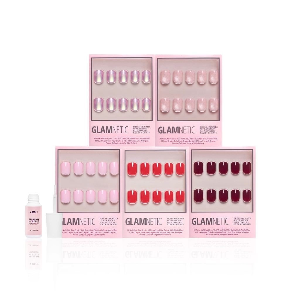 Six sets of glamnetic "The Super Short Edit" press-on nails in pink and red shades are shown in pink packaging, with a super short nail set and a small bottle of nail glue on the left, against a white background. - Product image