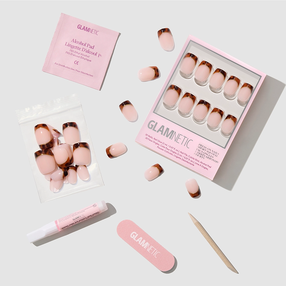 The Trendsetter press-on nails kit by glamnetic is arranged neatly, featuring short squoval tortoiseshell French tip nails, glue, alcohol pad, nail file, cuticle stick, plus extra nails in a resealable bag—all shown on a light gray background. - Product image