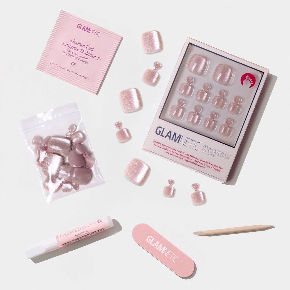 A flat-lay of the Glamnetic shimmery nude pink press-on toenail kit with nail prep tools and extra nails. - Product image