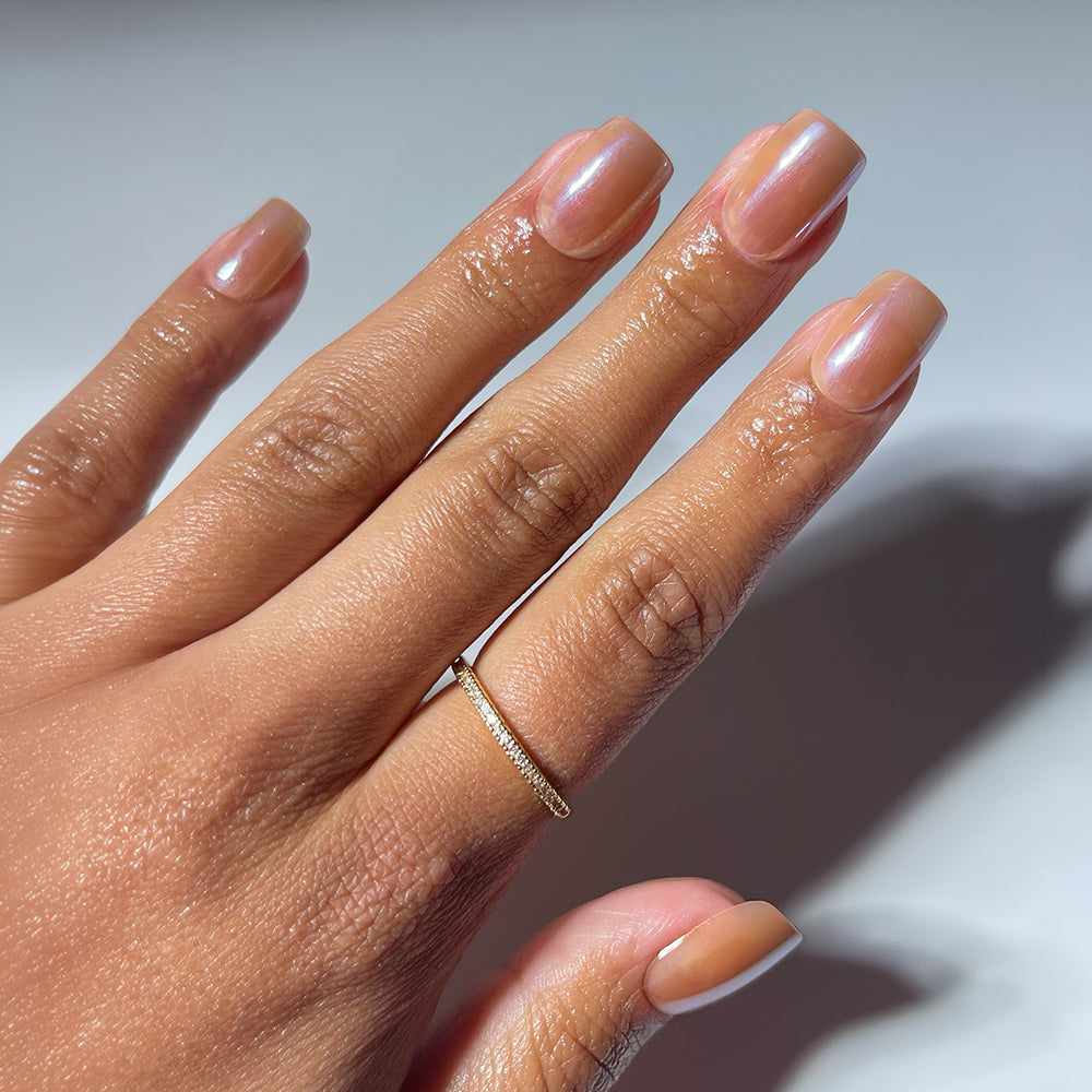 A hand with neatly manicured, short squoval nails wears glamnetic's THRILLA IN MANILA nude manicure and a delicate gold ring. The moisturized skin glows against a plain, softly lit background.