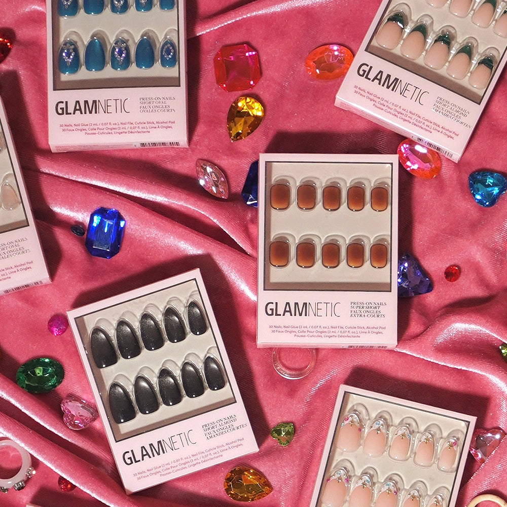 Boxes of glamnetic press-on nails, featuring the Tiger Eye style for salon-quality wear, are arranged on pink satin fabric and surrounded by colorful decorative gemstones. - Product image