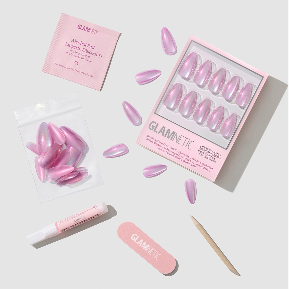 Timeless Oyster by glamnetic: a set of pink, pearlescent almond-shaped press-on nails with accessories—alcohol pad, nail glue, mini file, and cuticle stick—neatly arranged on a light surface.