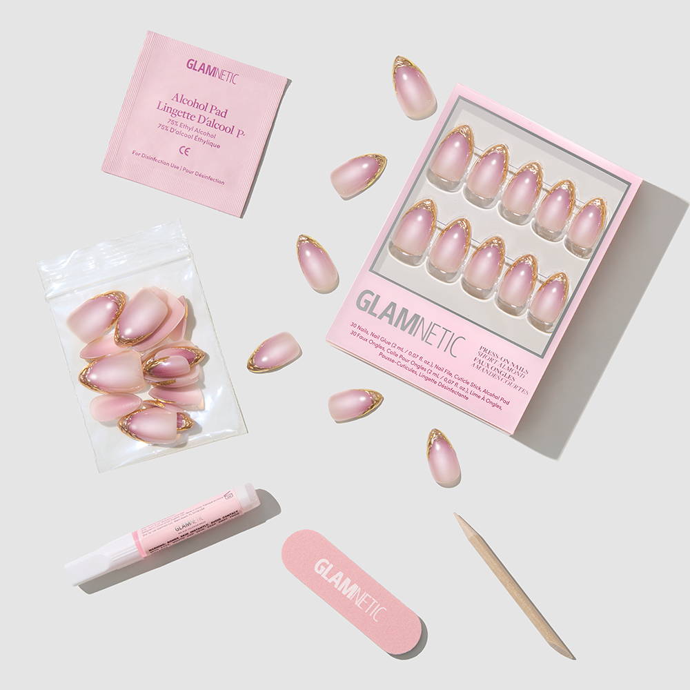 Glamnetic Tipped in Gold short almond press-on nails featuring a soft pink base with gold French tips, including nail glue, an alcohol pad, a nail file, and a wooden cuticle stick. - Product image