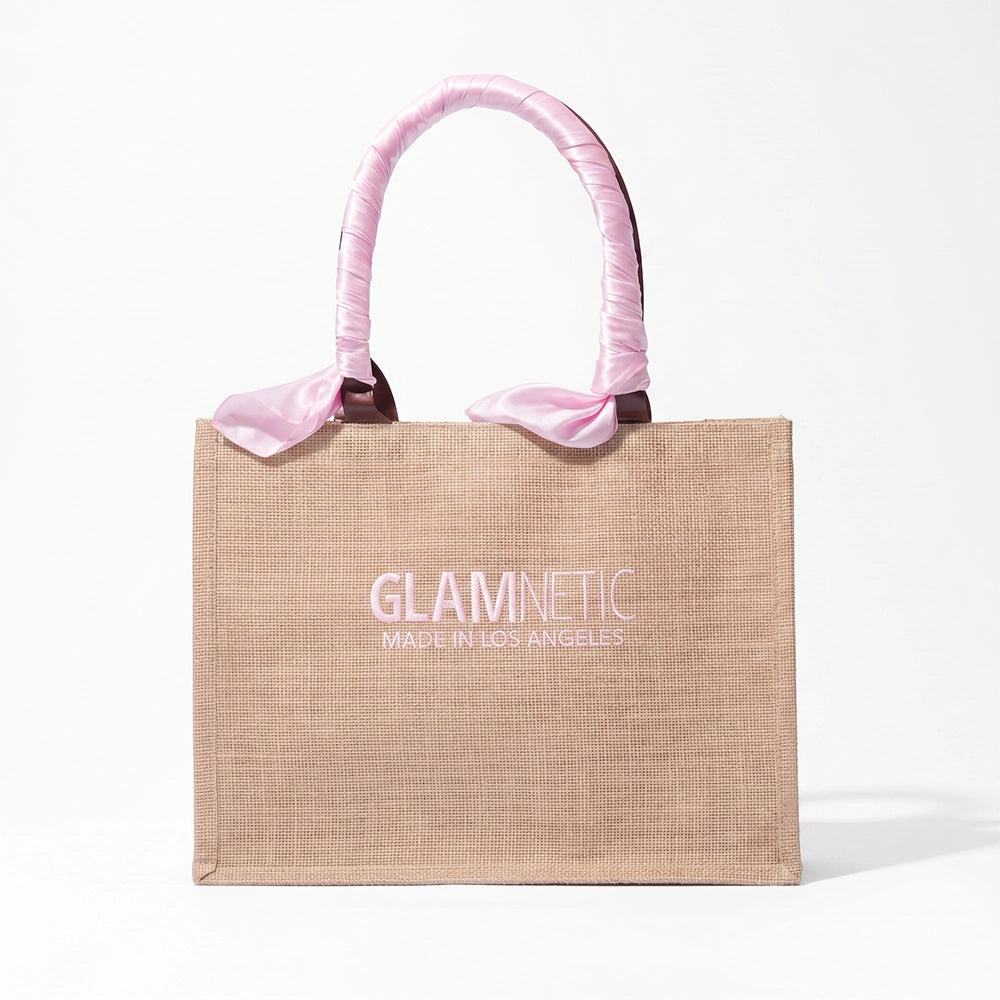The glamnetic Free Tote Bag ($85+ GWP) is a beige tote with "GLAMNETIC MADE IN LOS ANGELES" in white, plus pink fabric-wrapped handles tied in bows at the base, shown on a plain white background. - Product image