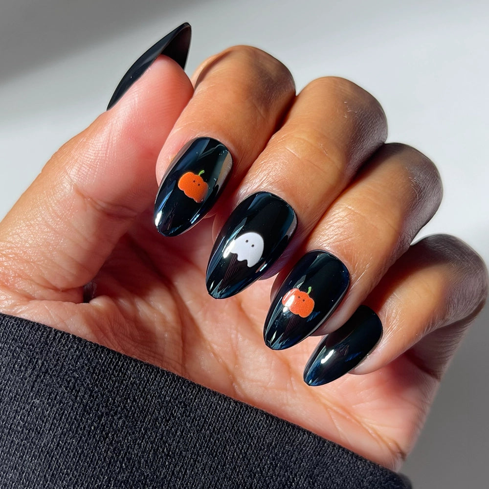 Get a close-up look at the glamnetic “Tricks &amp; Treats” press-on nails set, featuring long almond-shaped glossy black nails with a mesmerizing glazed finish. Some nails are adorned with charming Halloween-themed decals: an adorable orange pumpkin on the index and ring fingers, and a cute white ghost on the middle finger. Perfect for those who want an eye-catching, festive style—these press-ons offer effortless application for a gorgeous Halloween manicure.