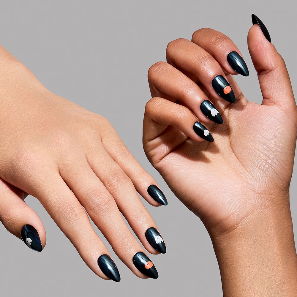 Two hands display the glamnetic Tricks & Treats press-on nail set, featuring long, almond-shaped nails painted in glossy black. Each nail is adorned with a chic glazed finish and small, round decorative accents, including a few bright orange dots among elegant white and silver details—adding an extra touch of sophistication to this striking look. - Product image