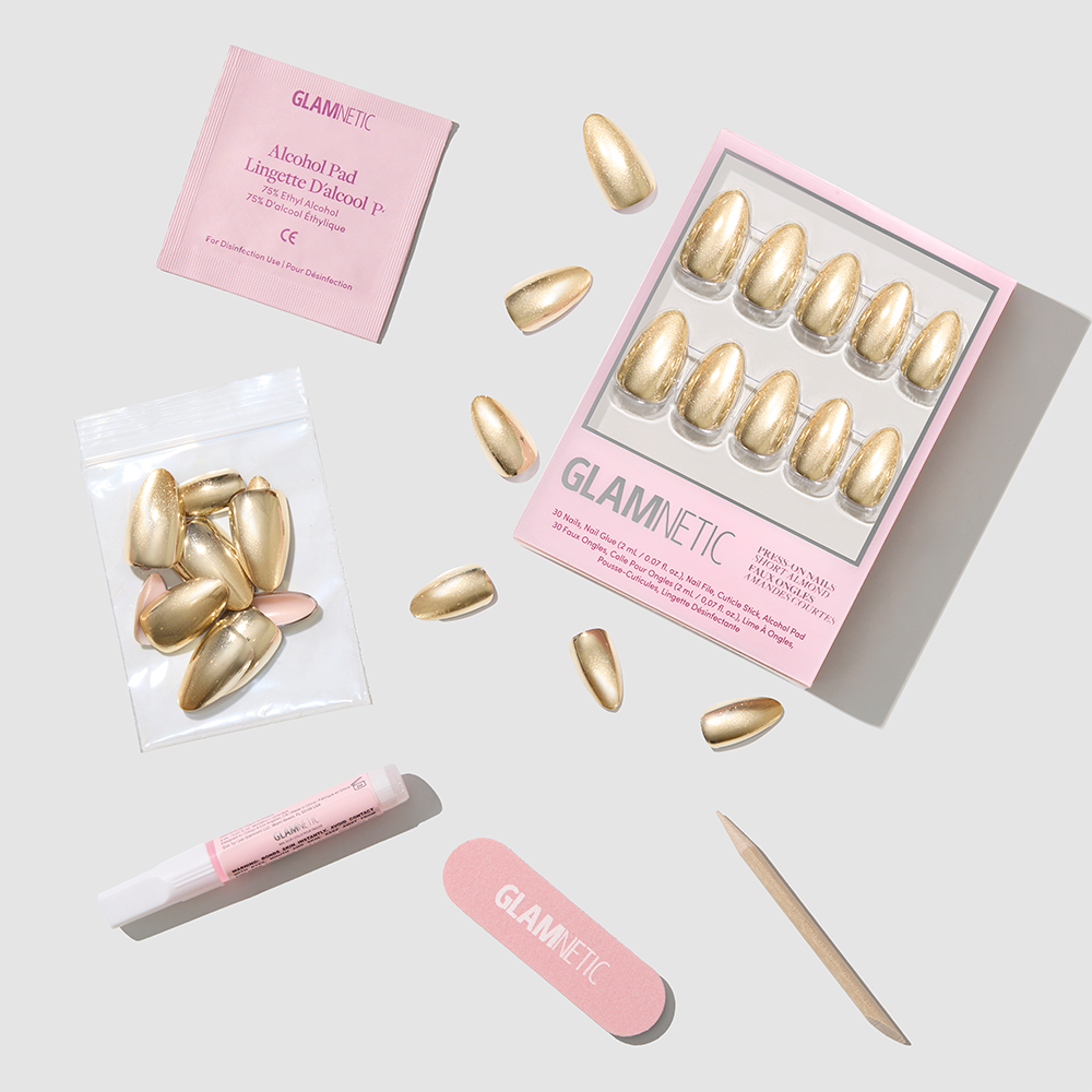 Glamnetic Trophy Wives short almond-shaped gold chrome press-on nails, including a box of 30, a bag of extra nails, glue, an alcohol pad, a nail file, and a wooden cuticle stick. - Product image