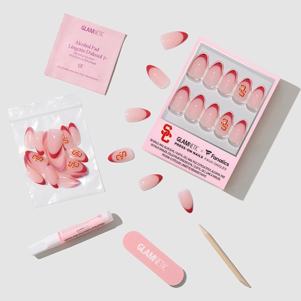 A flat lay of the glamnetic USC Trojans Press-On Nail Set with a box of red-tipped nails, loose press-ons, adhesive, pink nail file, cuticle stick, and alcohol pad on a light gray background. - Product image