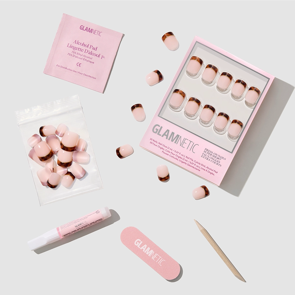 The glamnetic Unbothered set features super short pink and rose gold press-on nails, shown with nail glue, a cuticle stick, nail file, alcohol pad, and extra nails on a light gray background. - Product image