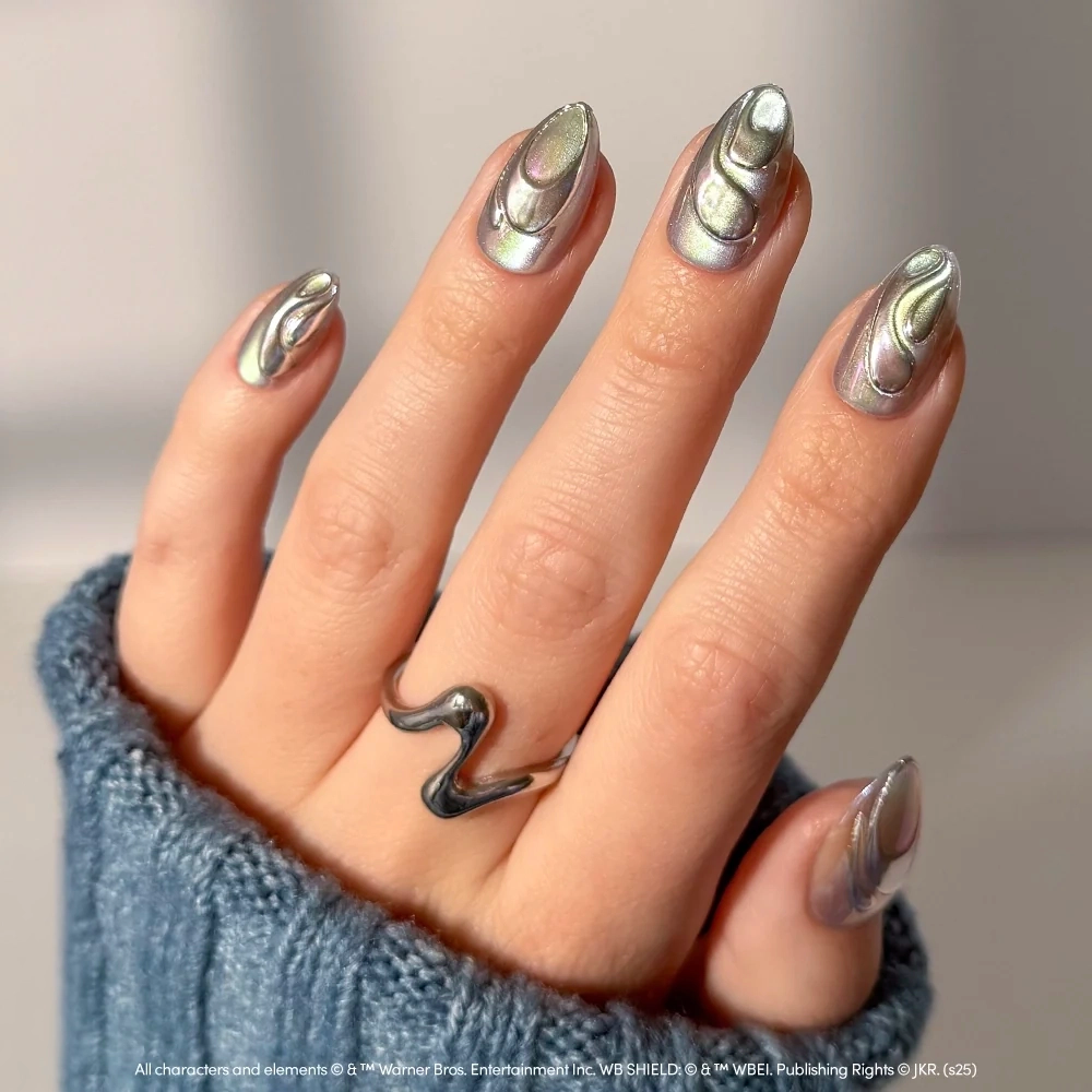 Glamnetic Unicorn Blood short almond-shaped chrome press-on nails with a metallic, iridescent finish and raised, swirling 3D designs, worn with a matching silver-toned wavy ring. - Product image