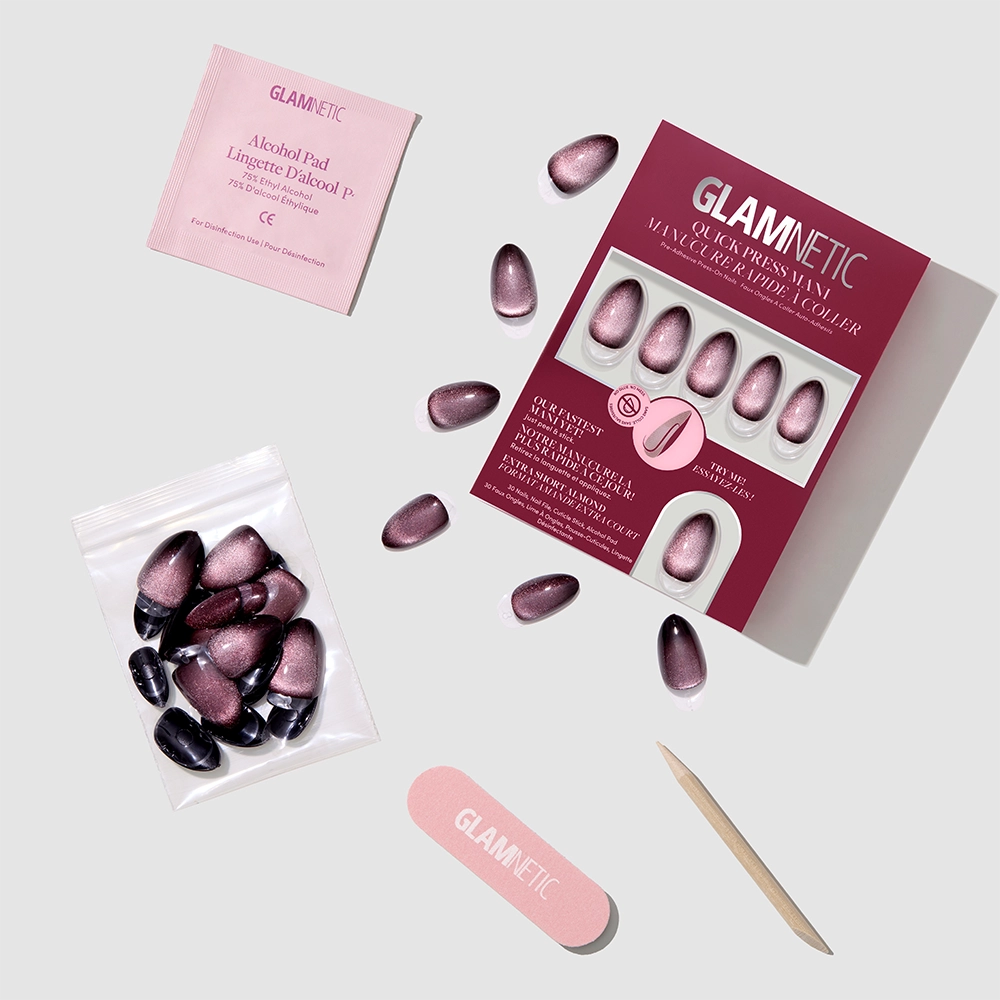 A box of glamnetic Velveteen Trance pink and black stick-on nails, complete with an alcohol pad, small nail file, cuticle stick, extra loose nails, and a packet, arranged on a light background. - Product image
