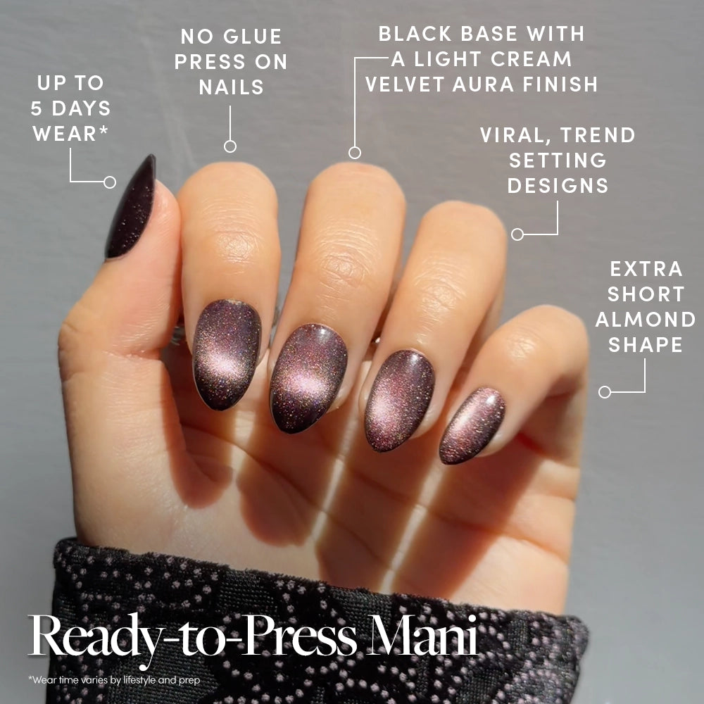 A hand with extra short, almond-shaped Velveteen Trance press-on nails by glamnetic, featuring a black base and a light cream velvet aura finish—these trendy, long-lasting, no-glue nails are ready to press for effortless style. - Product image