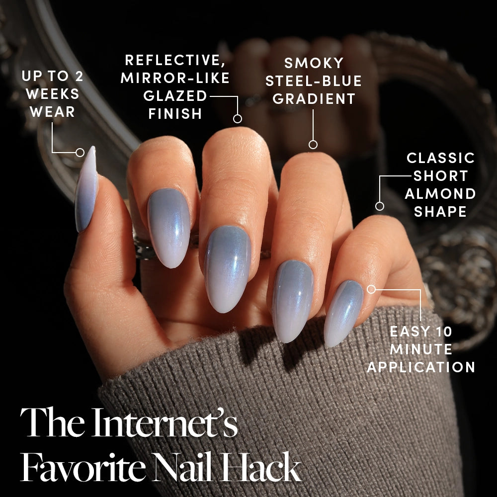 A hand wearing glamnetic’s Vintage Silver glazed nail set, featuring a short almond shape with a smoky steel-blue gradient and mirror-like finish. Enjoy 2-week wear, an ultra-glazed look, steel-blue ombré, chic almond tips, and a 10-minute application. The Internet’s Favorite Nail Hack. - Product image