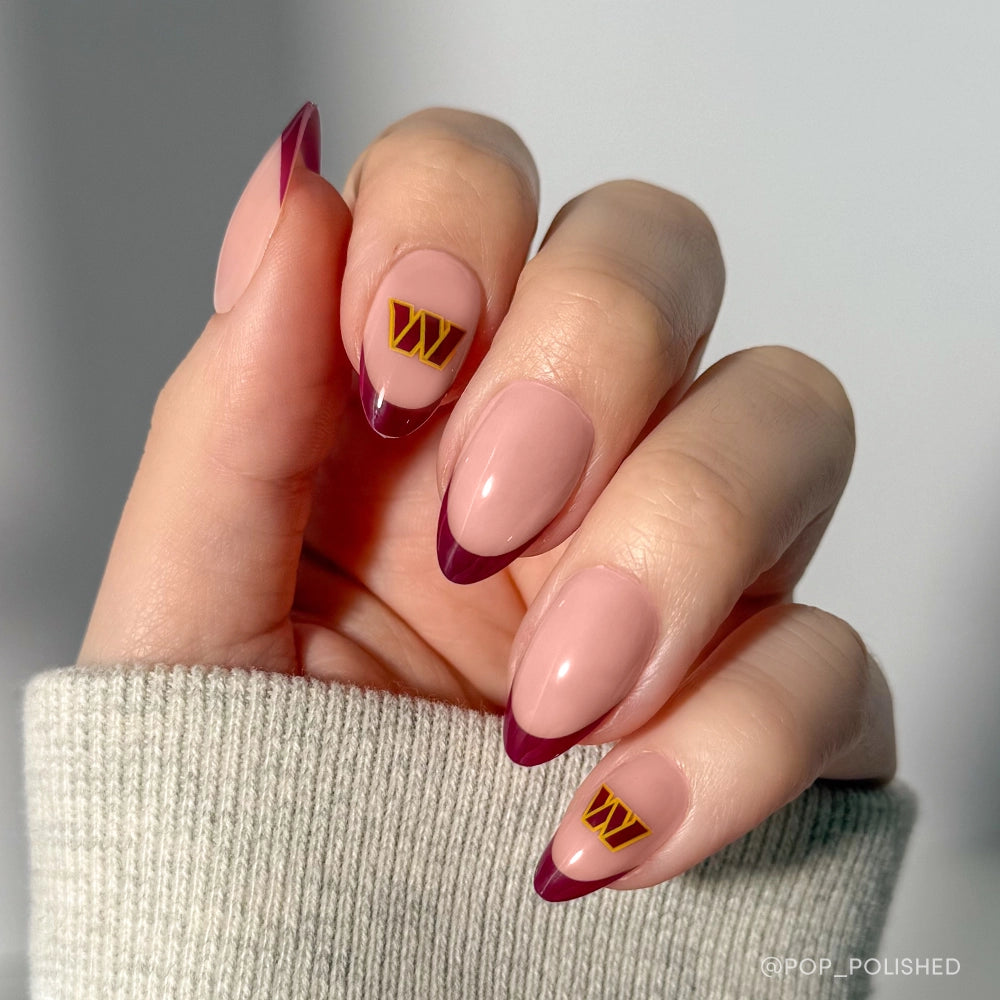 Show off your team pride with glamnetic’s Washington Commanders Press-On Nail Set—almond-shaped nails with a nude base, burgundy French tips, and gold W accents. Paired here with a light grey ribbed sleeve for the perfect fan look.