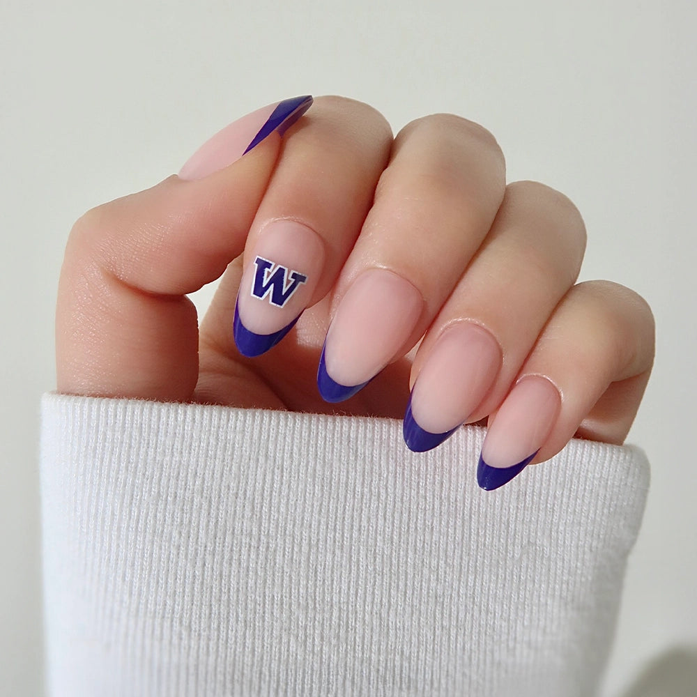 Show your team spirit with the glamnetic Washington Huskies Press-On Nail Set—almond-shaped nails with a nude base, purple French tips, and a W decal on the ring finger. Perfect for game day! Styled here with a white long sleeve shirt. - Product image