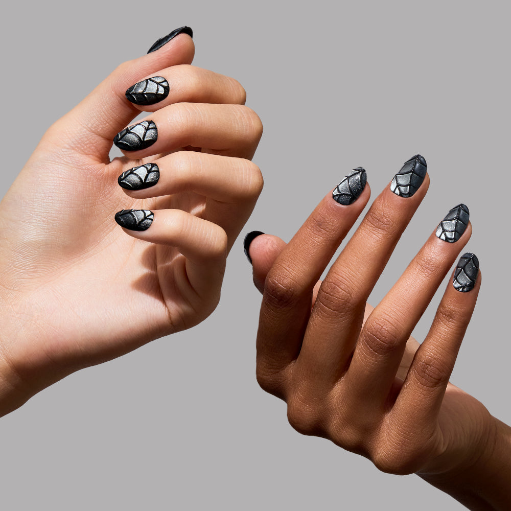 Two hands with different skin tones are displayed against a gray background. Both have almond-shaped, short oval nails featuring a textured, 3D black-and-silver spiderweb pattern reminiscent of luxurious black velvet nails. - Product image