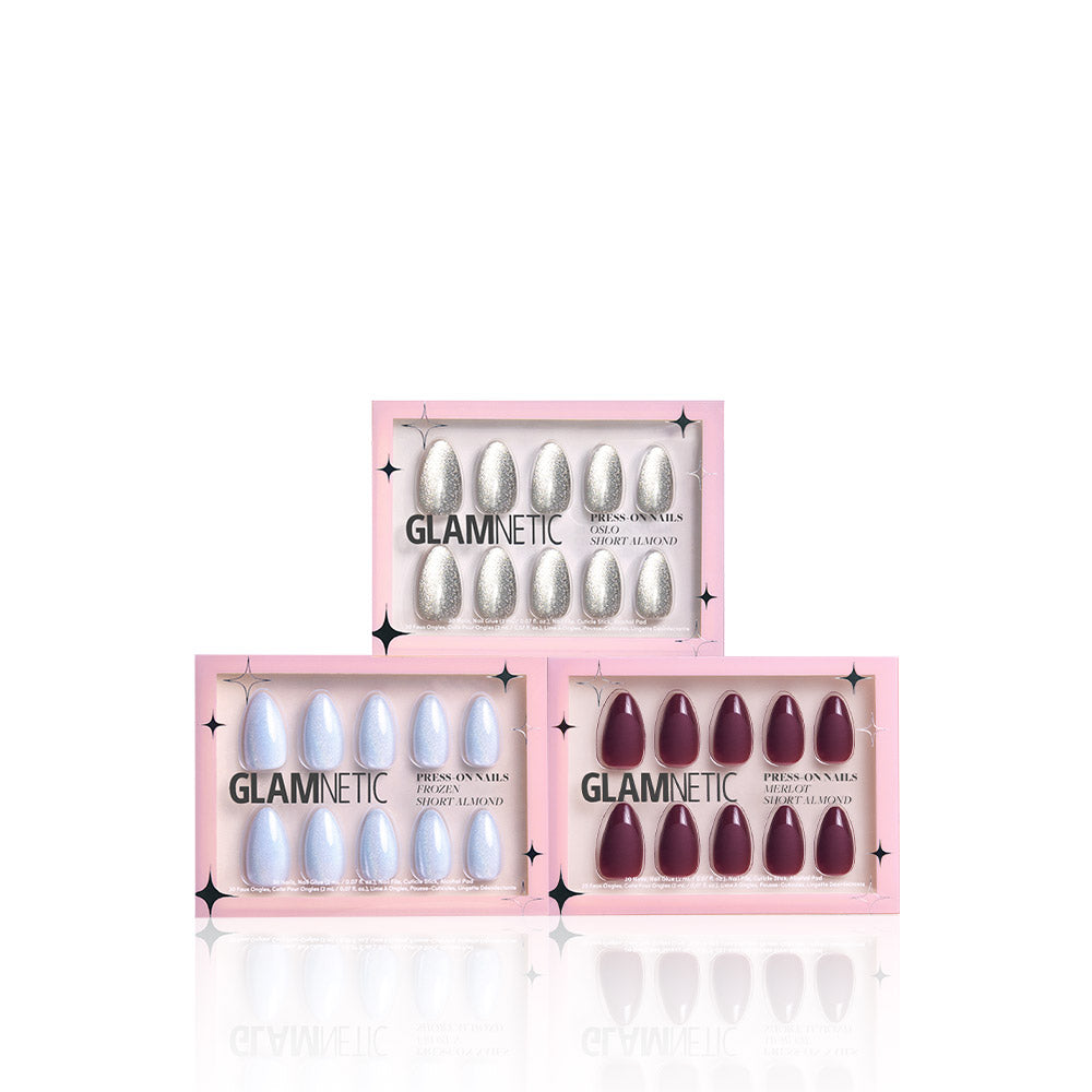 Three boxes of glamnetic Winter Wonderglam almond nail sets are stacked in a pyramid, showcasing silver glitter, light blue cat’s-eye shimmer, and deep burgundy styles. The chic pink packaging highlights these reusable nails. - Product image